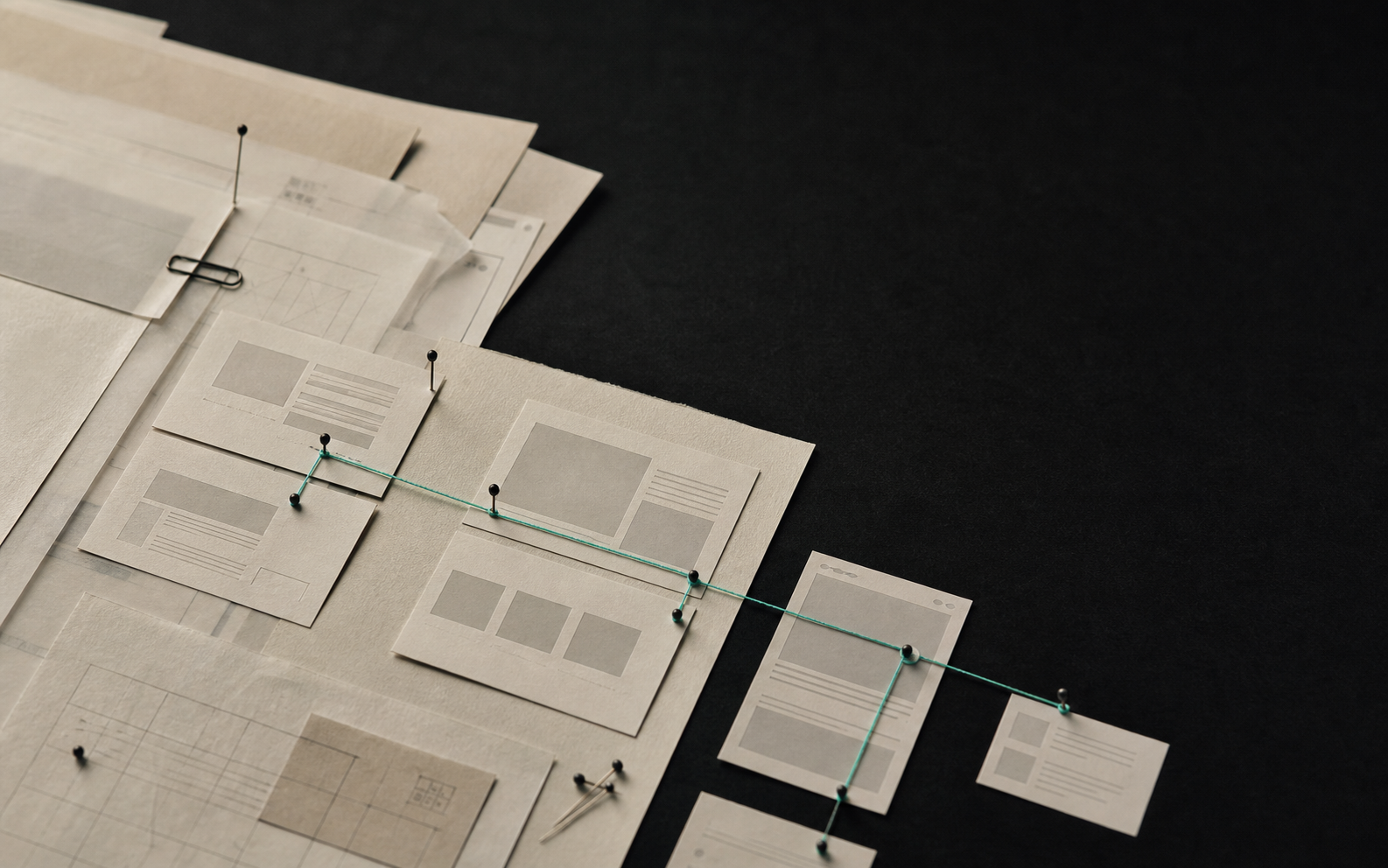 Layered cream paper sheets and modular web-layout cards pinned in a grid, with a thin teal thread connecting them like a build pipeline.